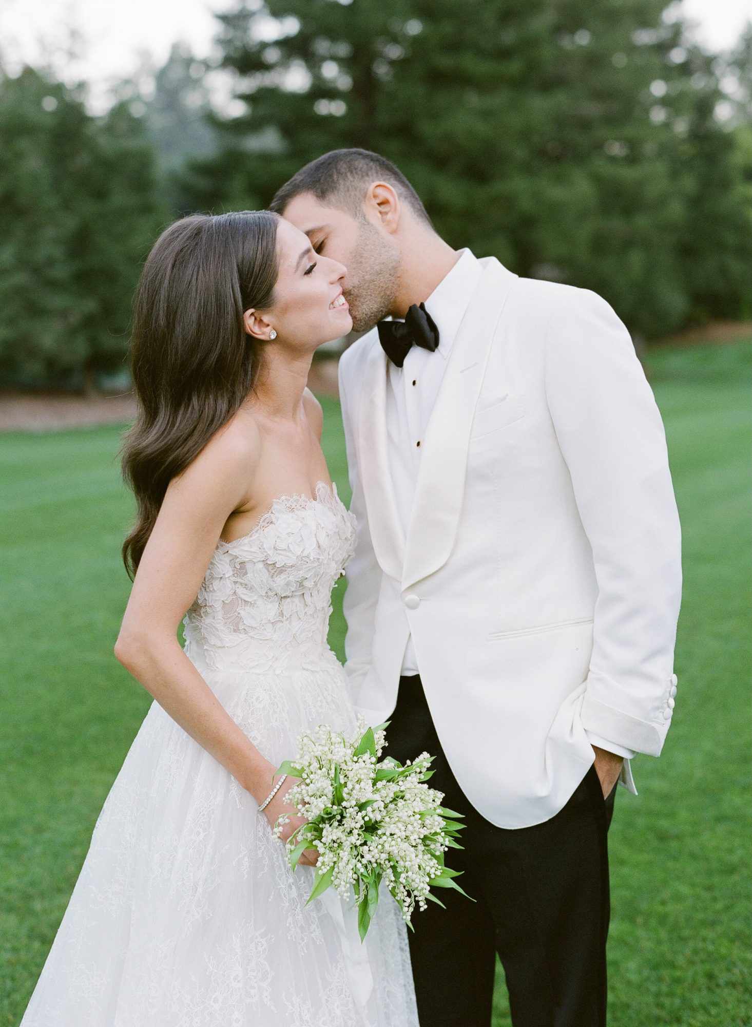 groom kisses bride outdoors in white wedding attire