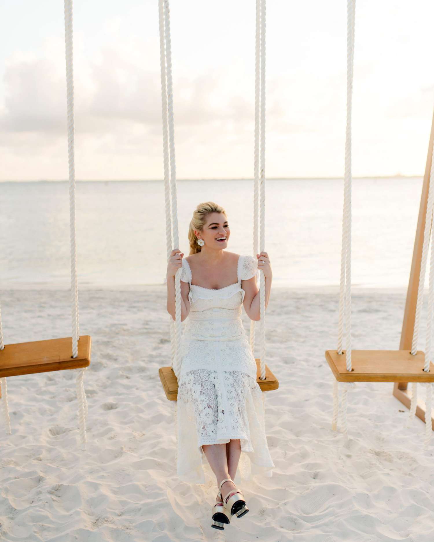 bride sitting on wood and rope swing set on beach
