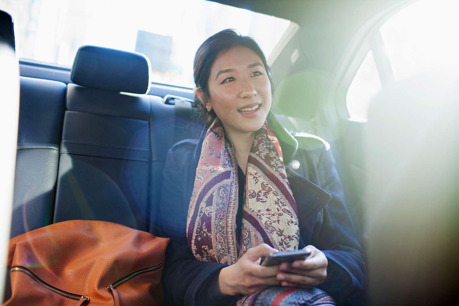 Young asian business woman looking at smartphone sitting in car service limousine