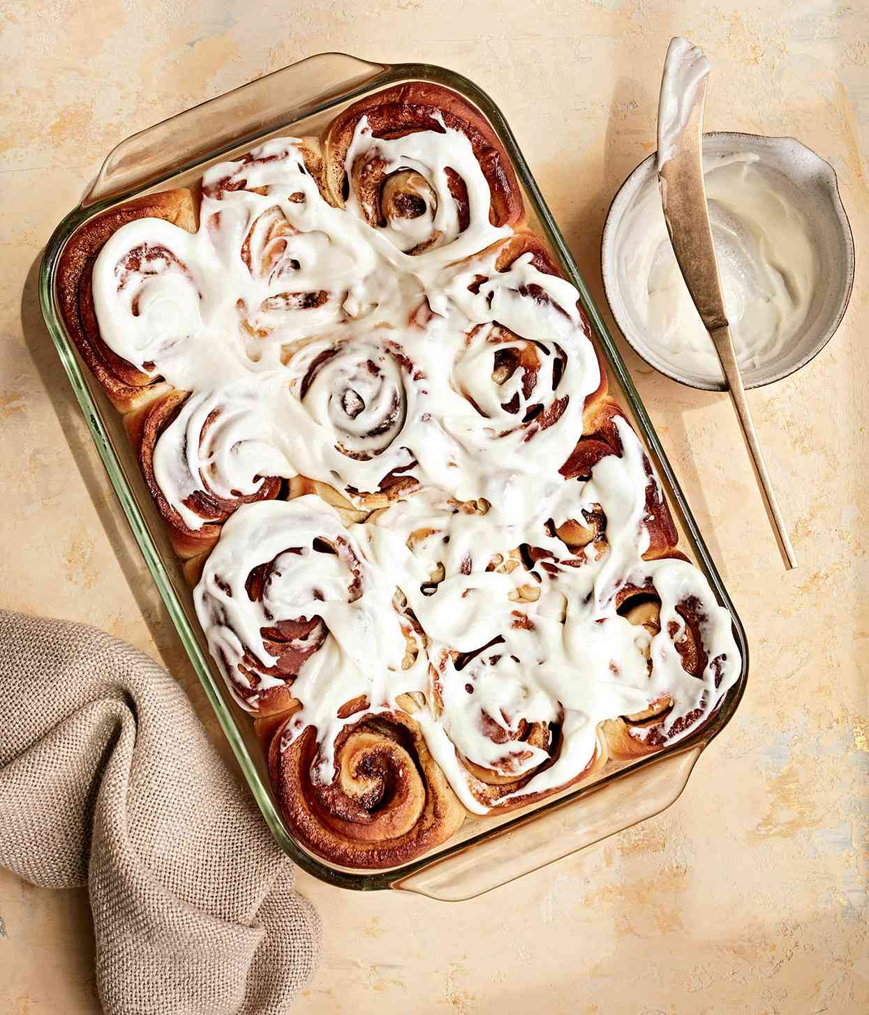 cinnamon rolls in glass pan with bowl of frosting