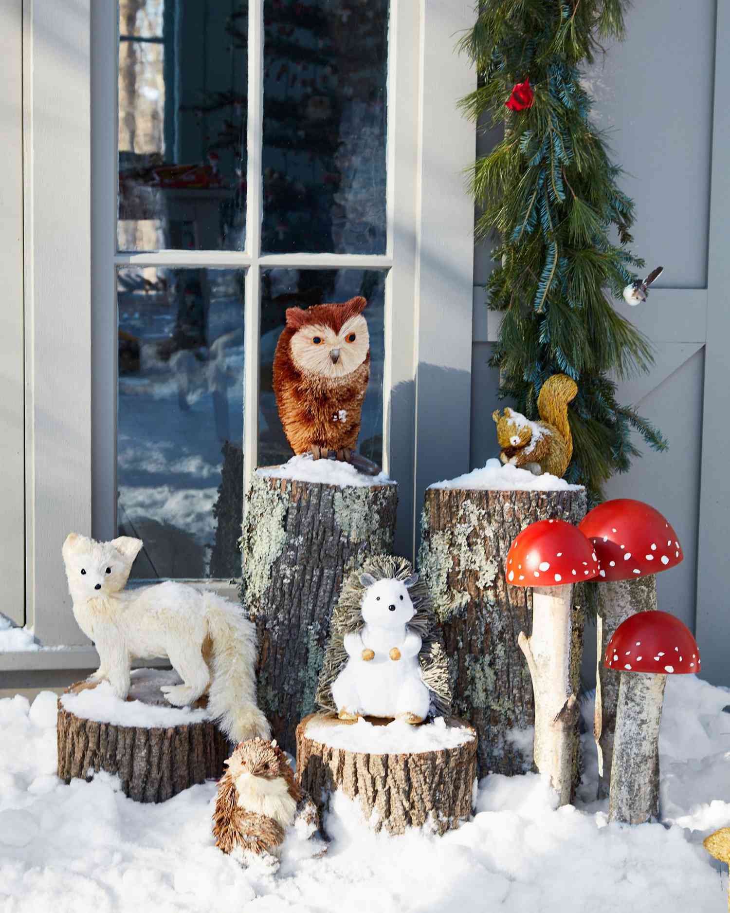 various woodland creatures on snowy logs outside cottage