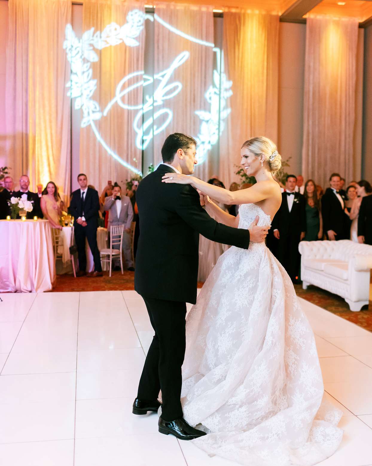 bride and groom share first dance on white tile dance floor surrounded by guests