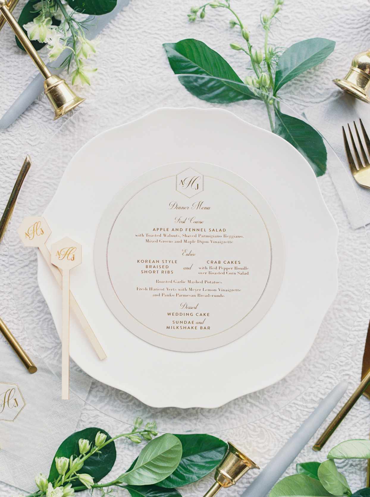 wedding reception menu with gold writing on white place setting with greenery accents