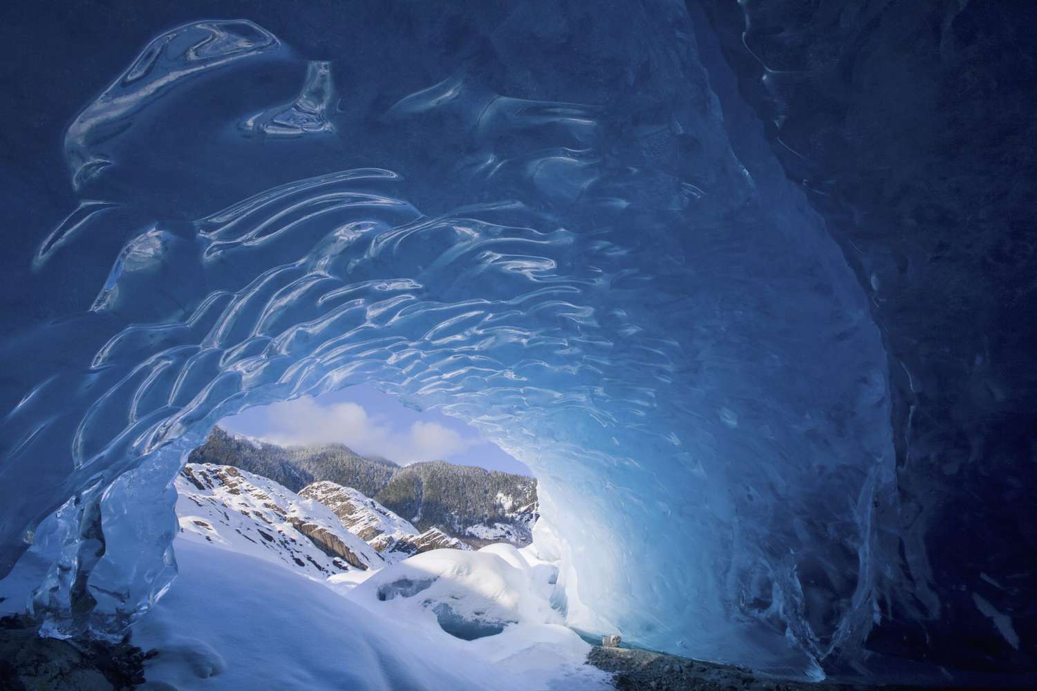 view from inside an ice cave looking outward at the snow-covered landscape mendenhall glacier near juneau in Alaska