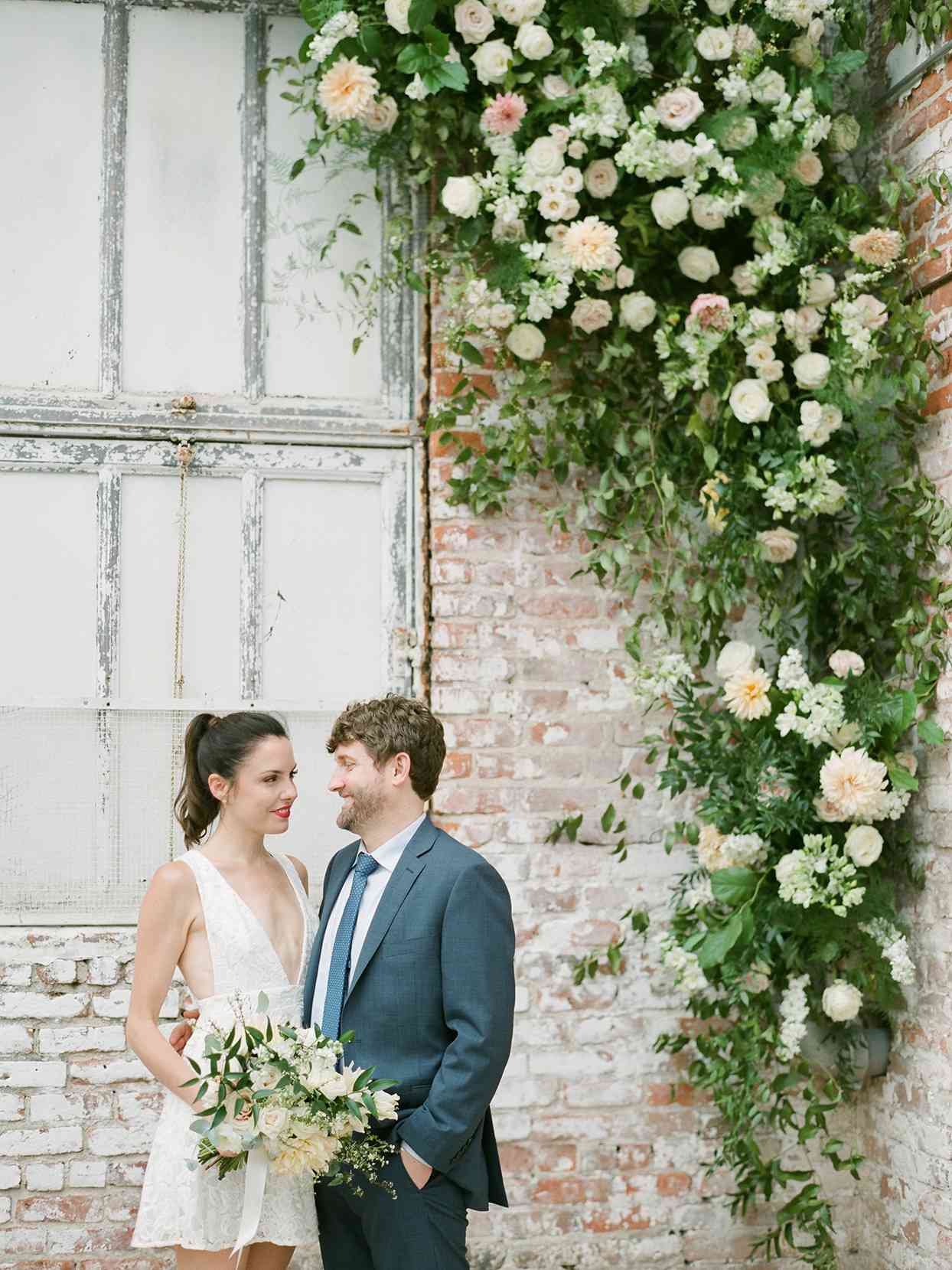 Wedding couple standing in front of brick wall with flowers