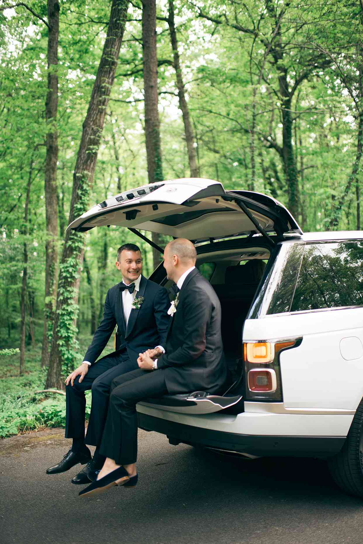 grooms sitting inside open tailgate of car in the forest