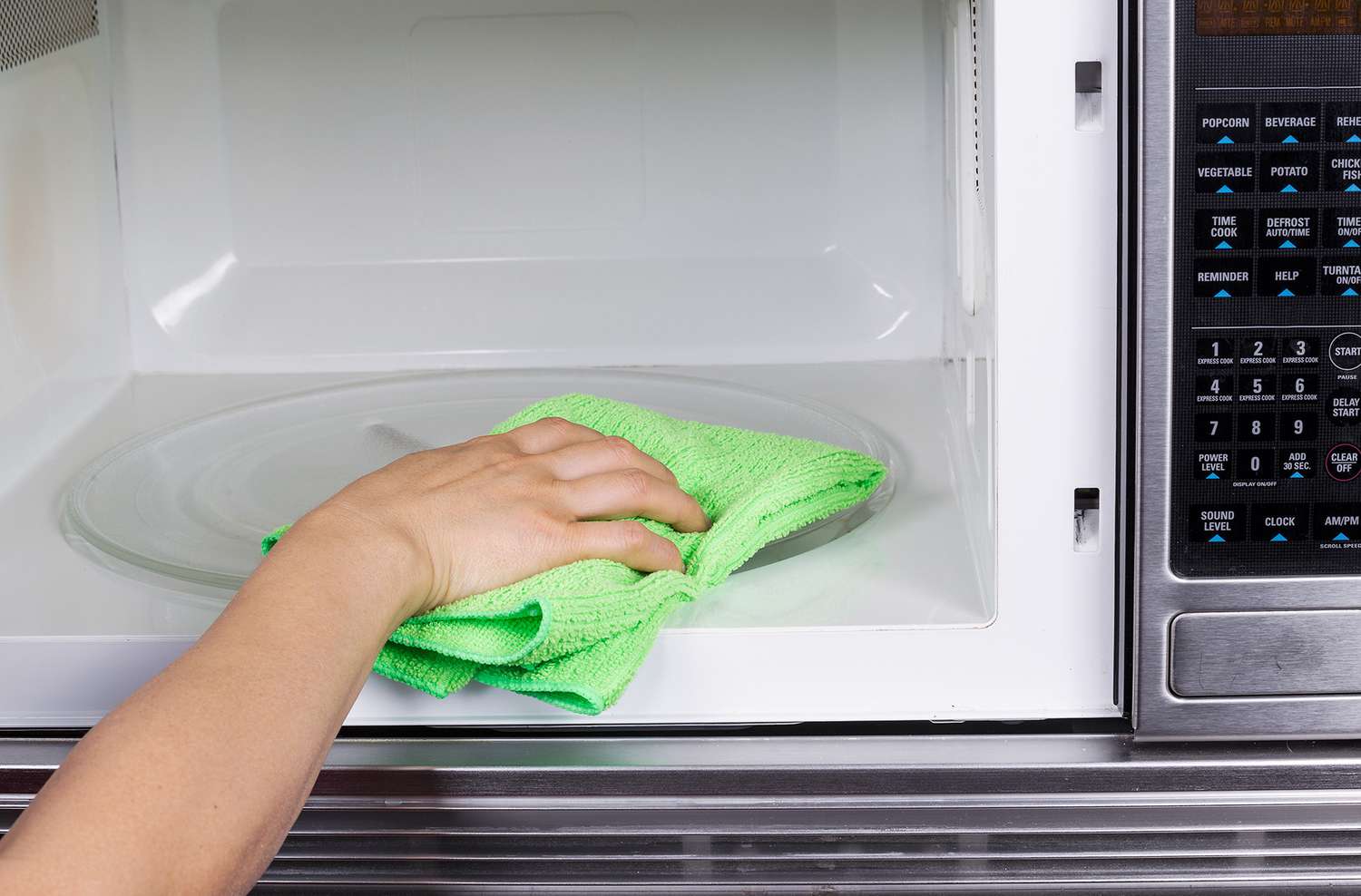 Hand with microfiber cleaning rag wiping inside of microwave oven