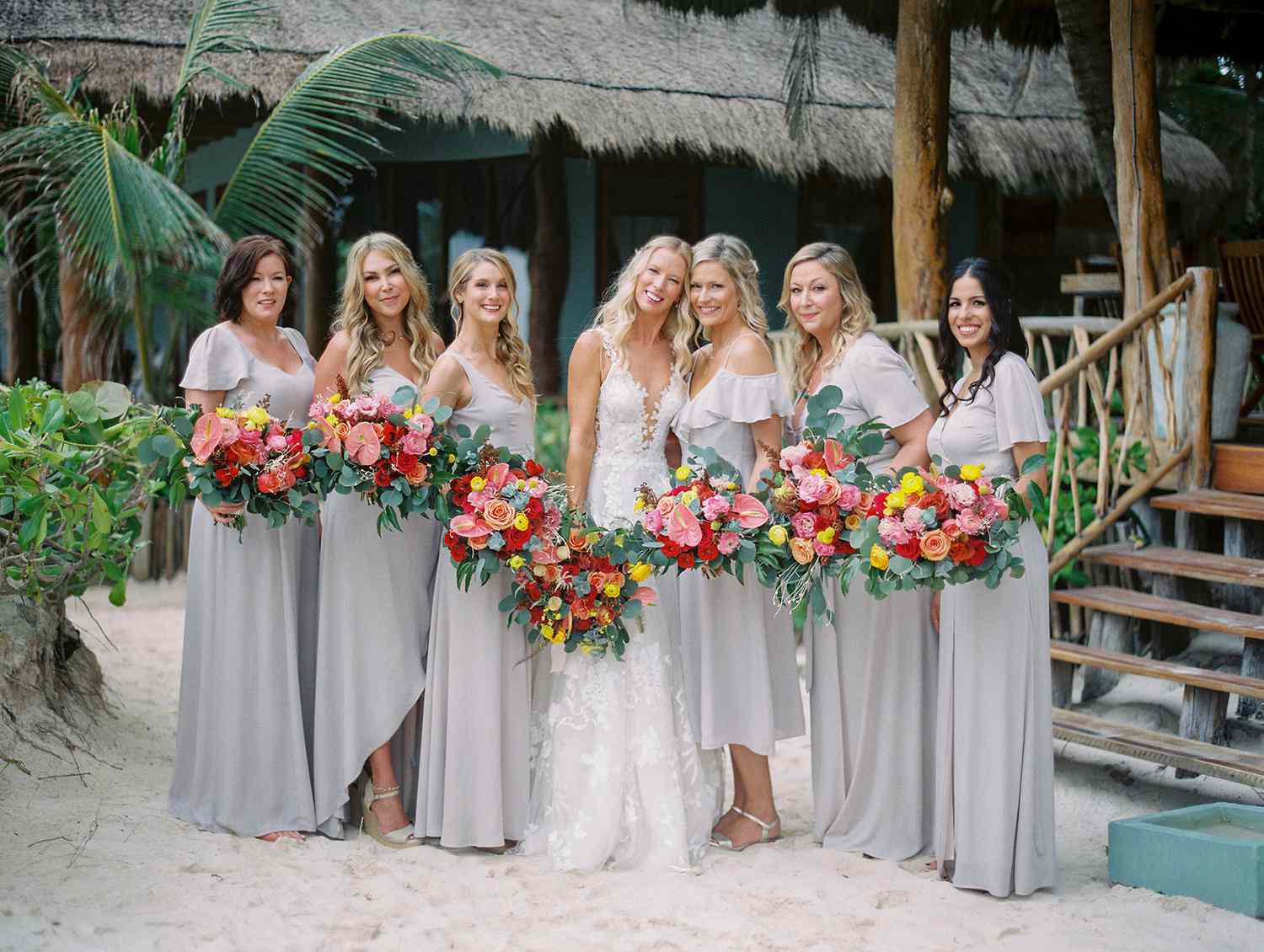 bride and bridesmaids in light gray holding red and yellow bouquets