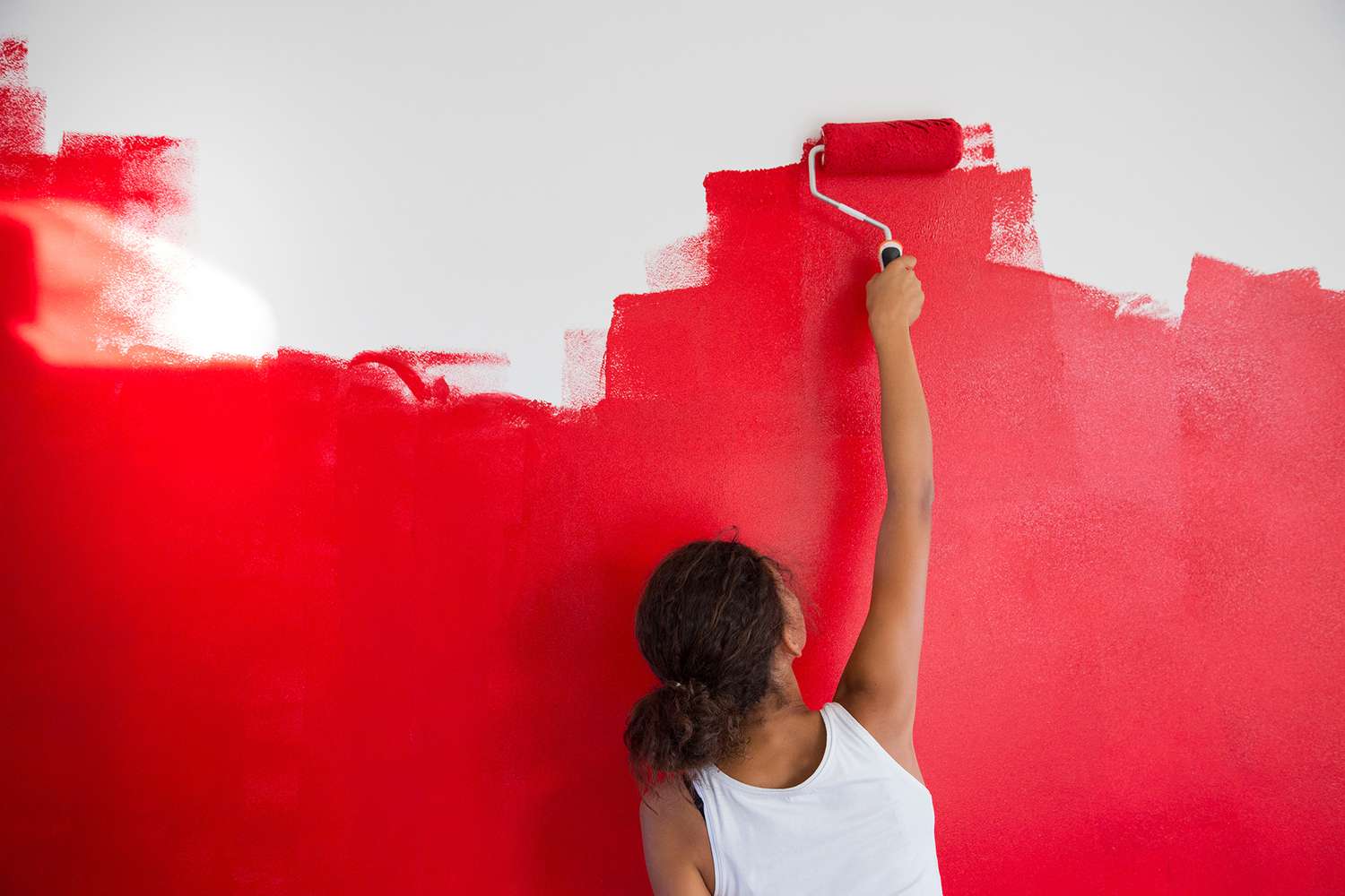 girl painting red wall with paint roller