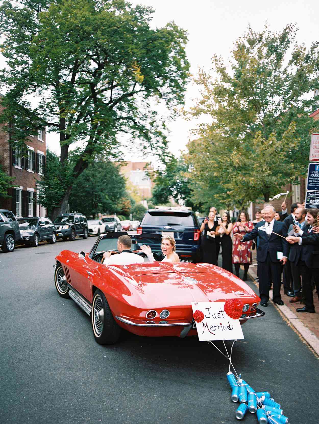 bride and groom driving away in just married car