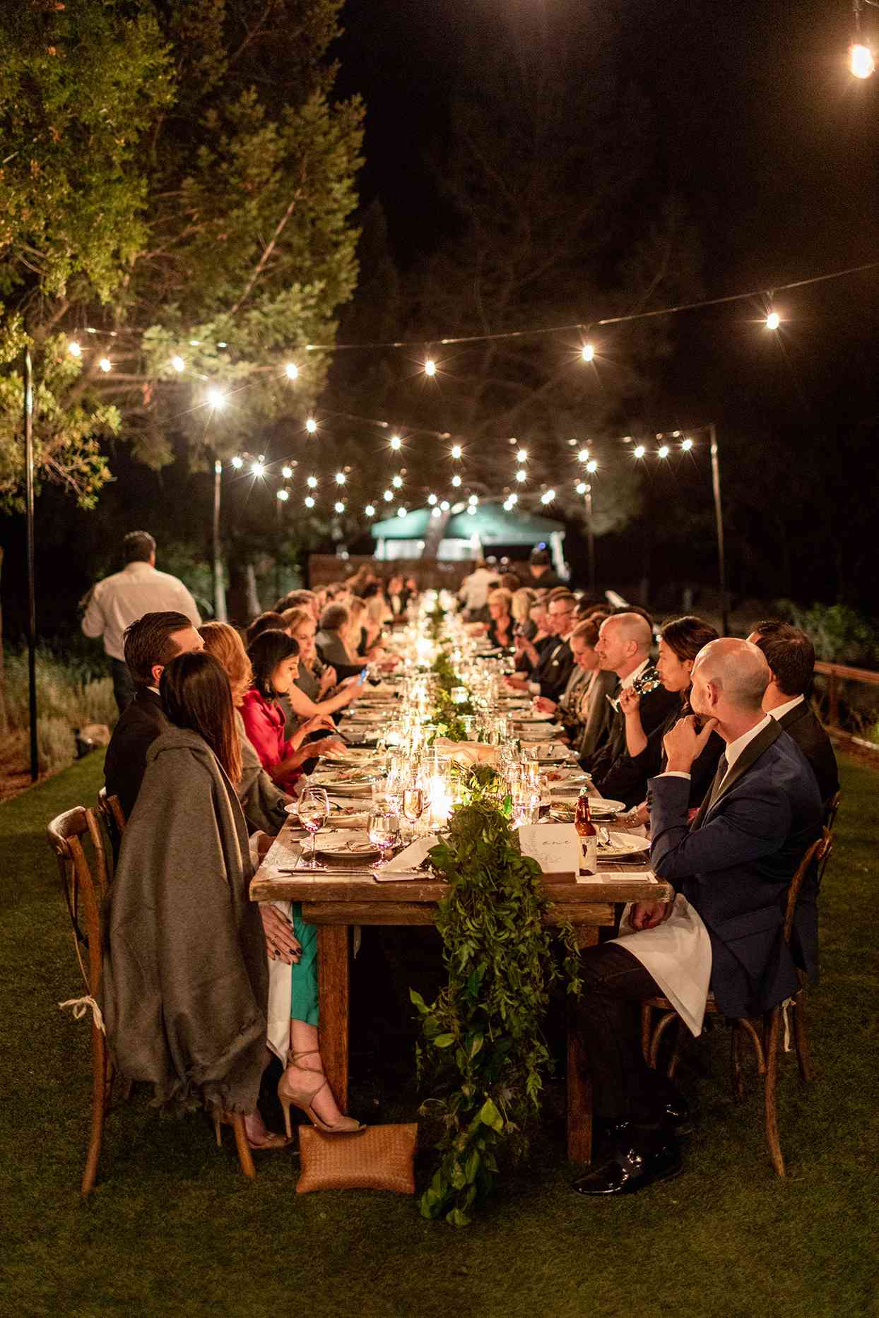 guests eating at evening reception elegant long table under string lights