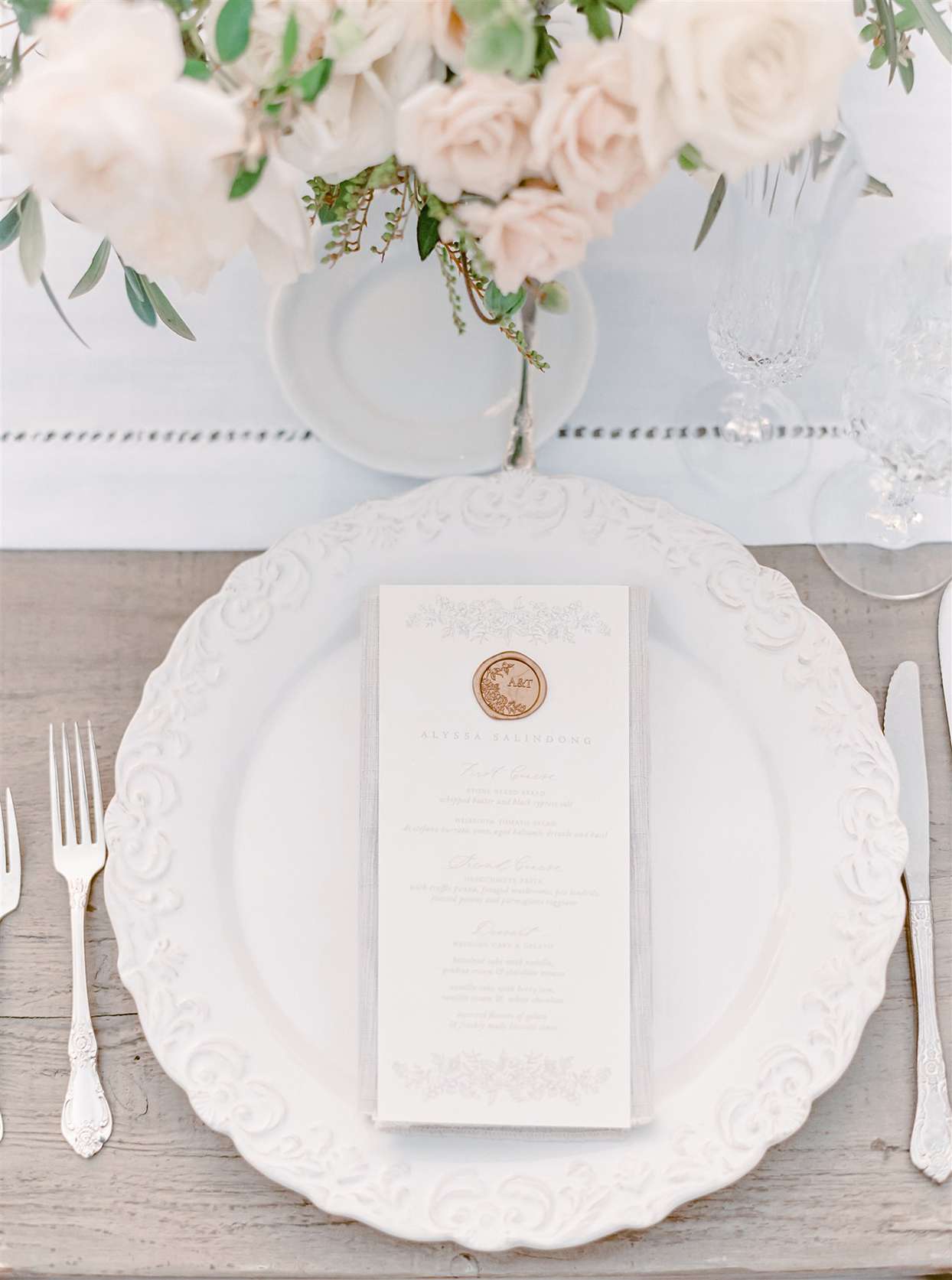 Place setting with white ceramic chargers with a vintage-inspired textured border, silver flatware, and crystal stemware