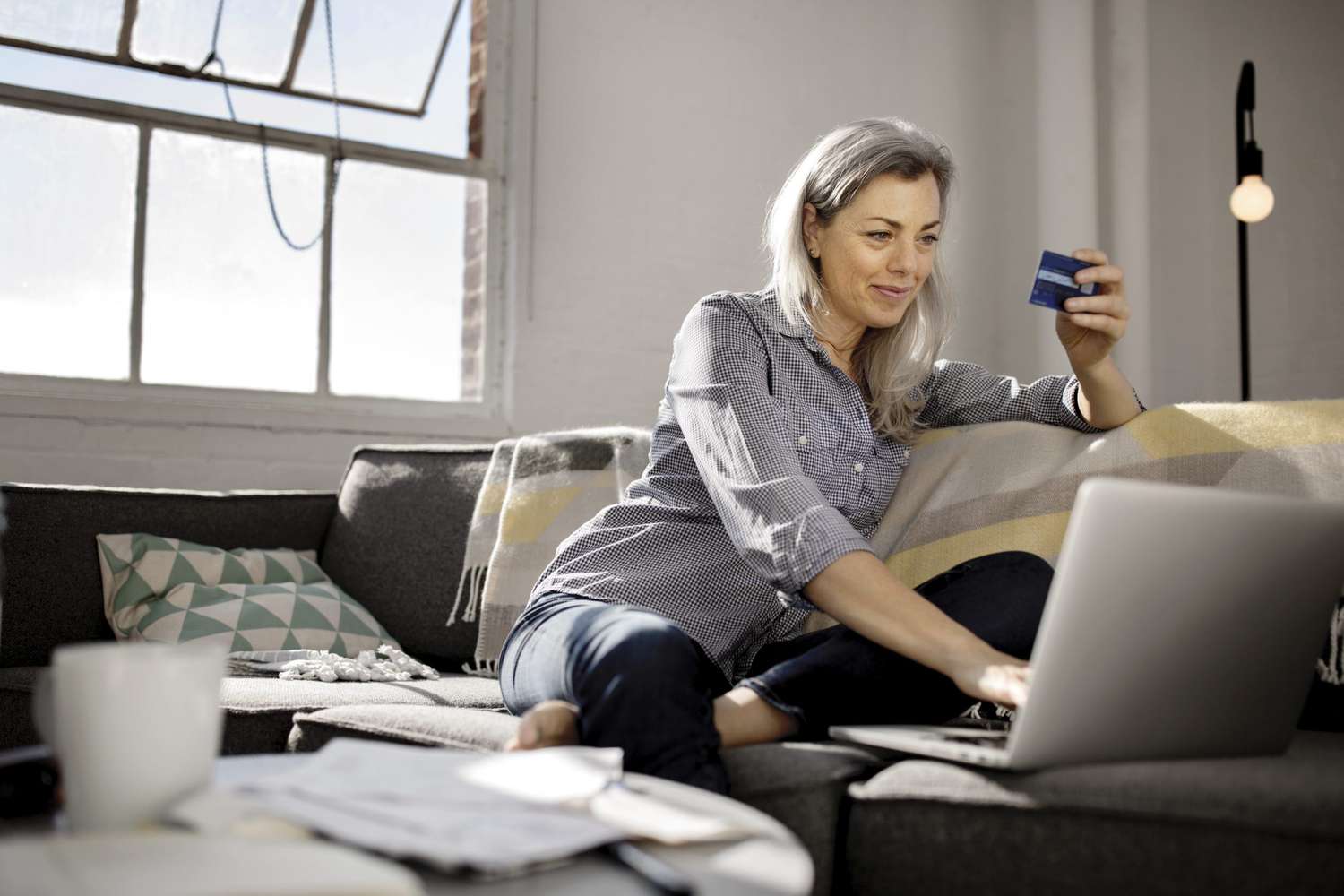woman holding debit card while using laptop on sofa