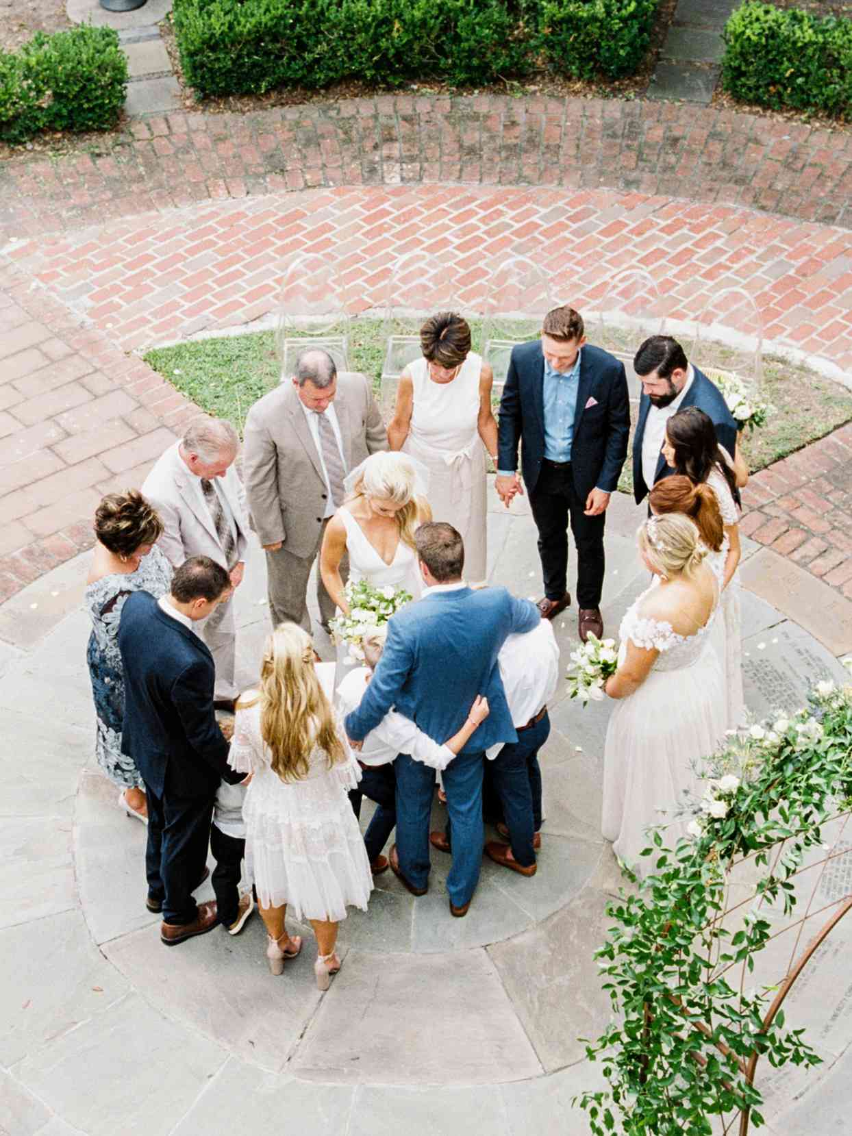 bride and groom surrounded by family in prayer circle