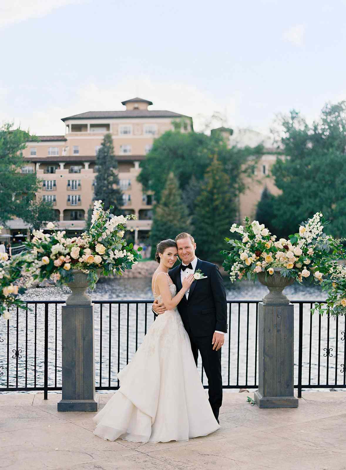 couple posing on terrace between floral urns in front of water