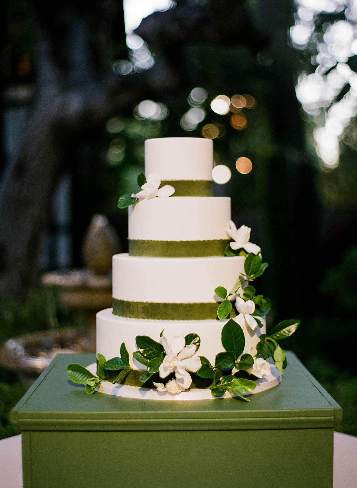 four tiered white wedding cake with green ribbons and flowers
