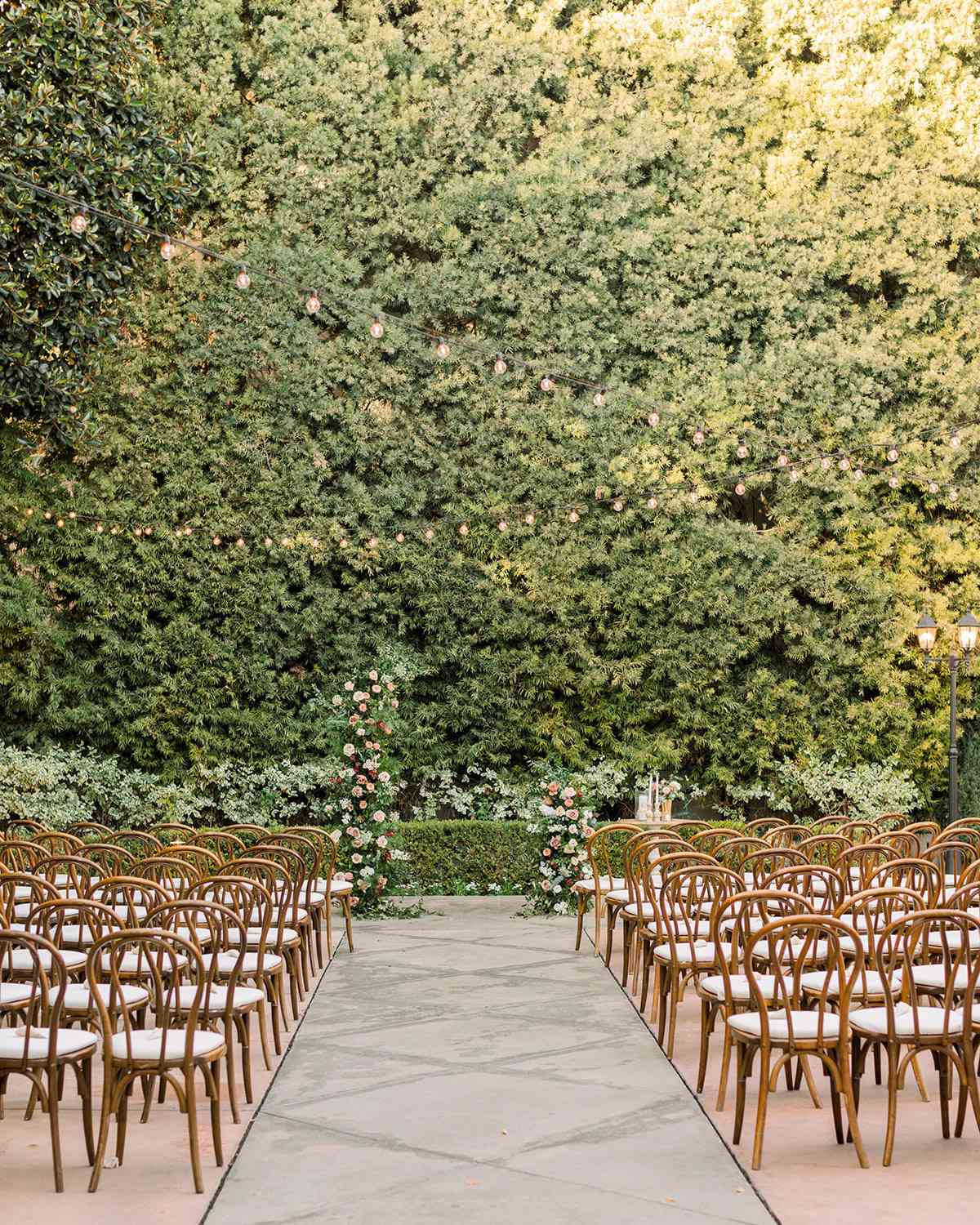outdoor ceremony location with greenery wall and wooden chairs