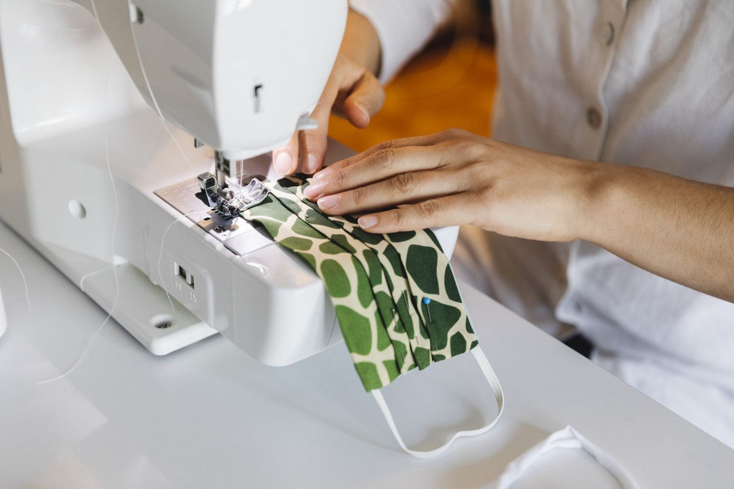 woman sewing green protective face mask on sewing machine