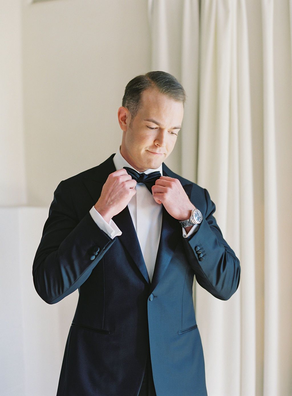 groom in black tux adjusting bowtie