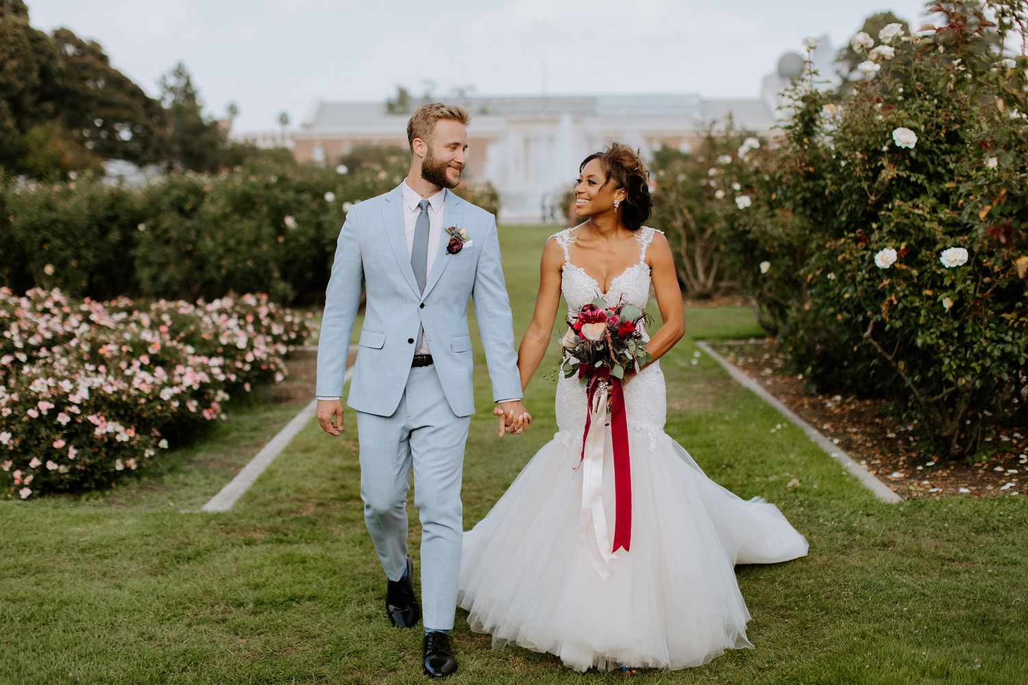 groom in pastel blue suit and bride in wedding dress walking in garden