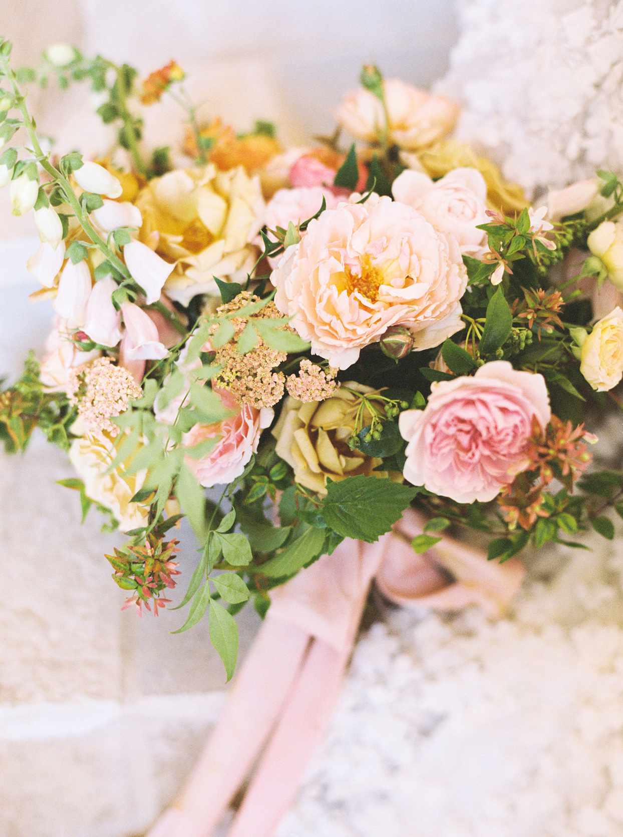 Wedding bouquet of ranunculus blossoms, dusty peach lisianthus blooms, and garden roses in hues of light gold and sand