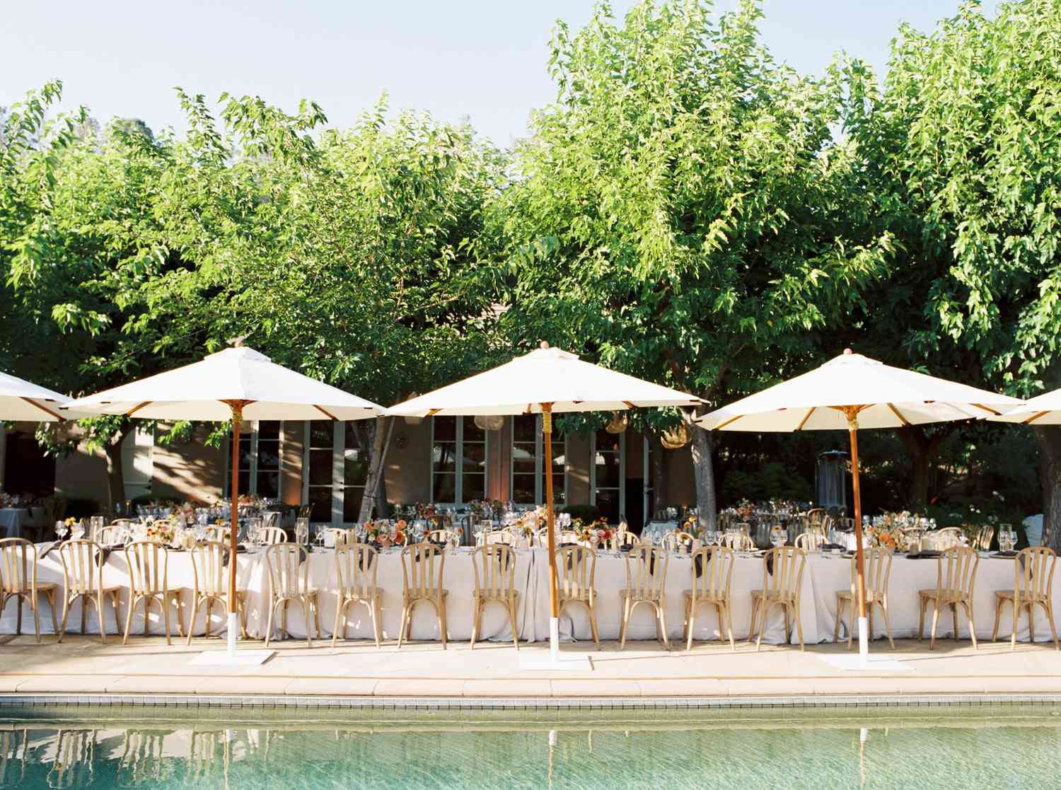 reception tables set up under umbrellas by pool