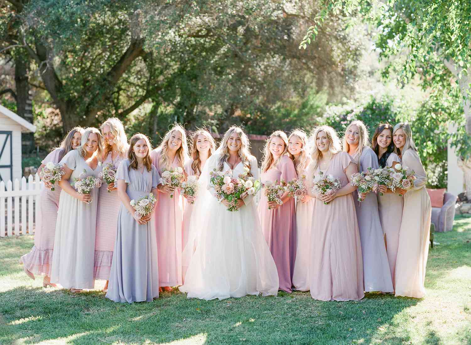 bride standing with 12 bridesmaids in various colored flowy dresses