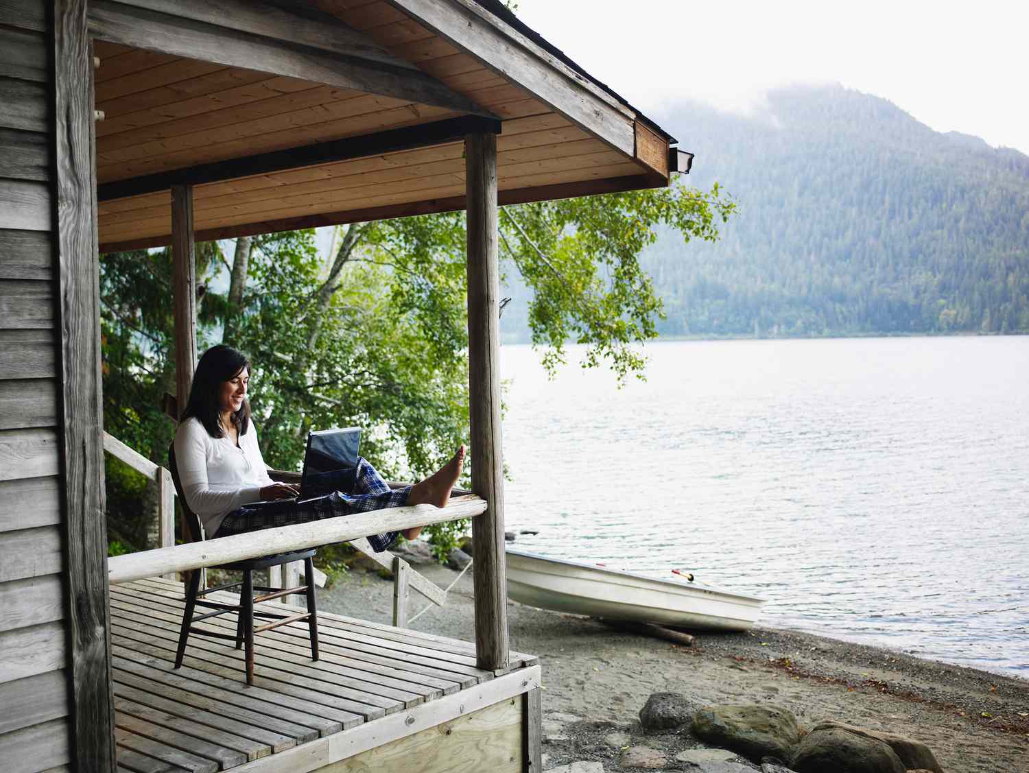 woman sitting on front porch by the lake with laptop