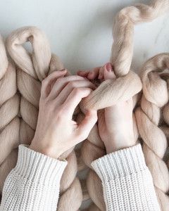 hand pulling yarn through loop for arm knit blanket