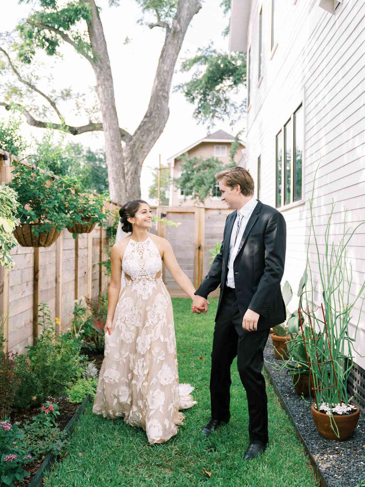 wedding couple holding hands and walking through small pathway on side of house