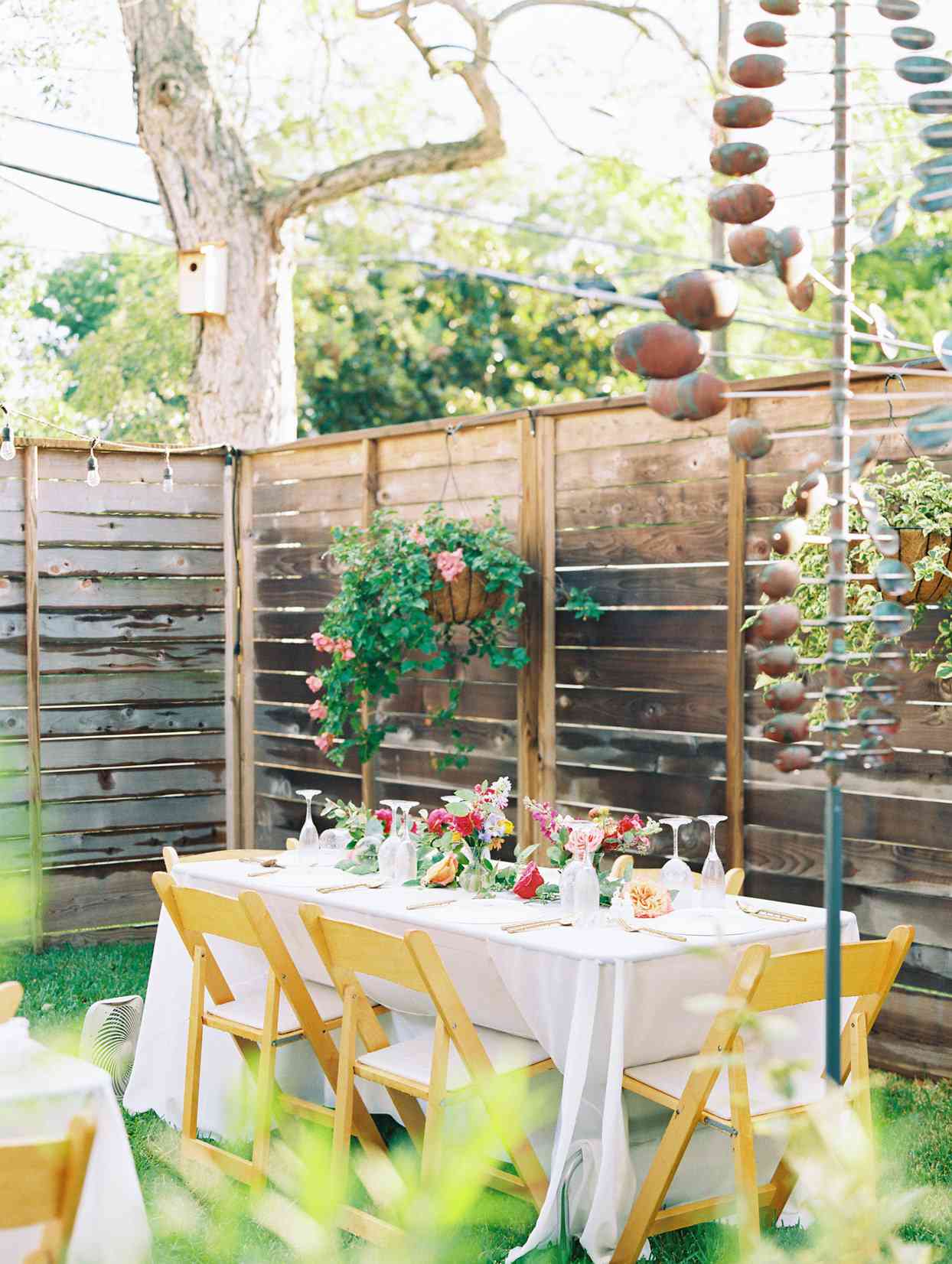 backyard wedding reception with white tables and wooden chairs