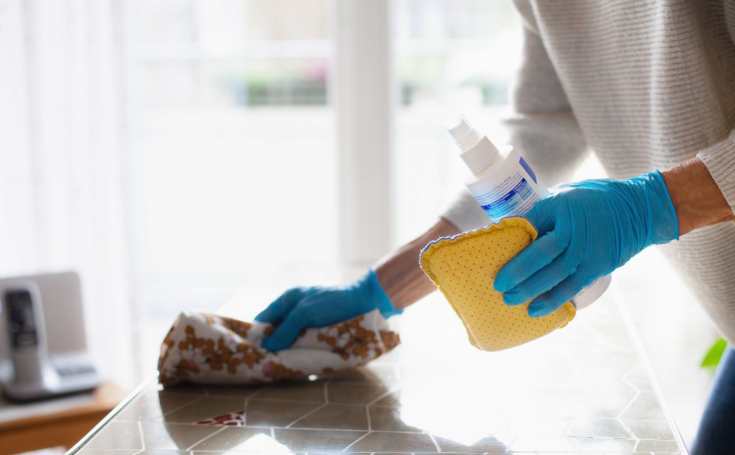 woman wearing blue gloves cleaning countertop with product and cloth