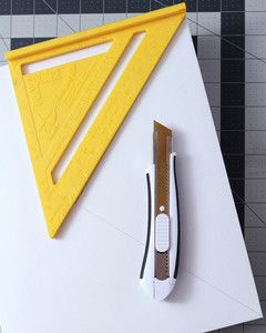 yellow speed square and utility knife atop white rectangular box