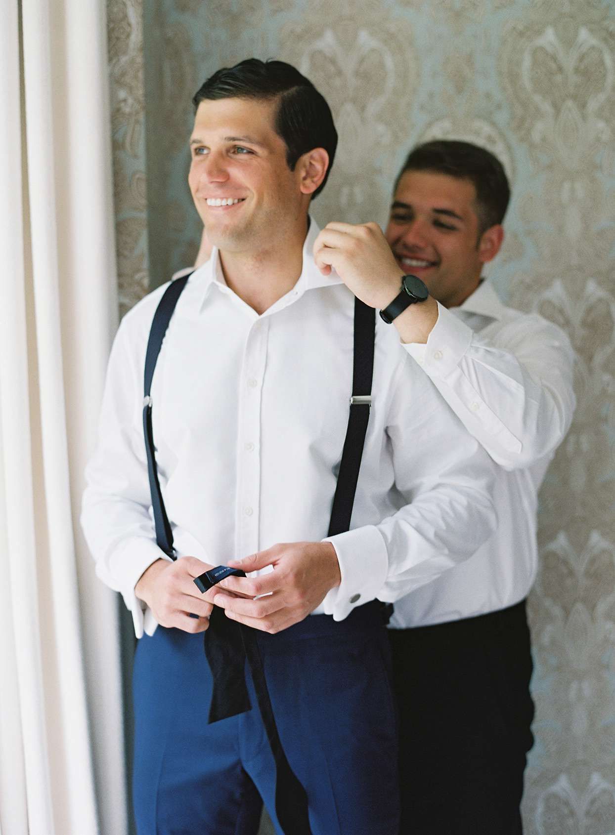 groom smiling while getting ready with groomsmen before wedding