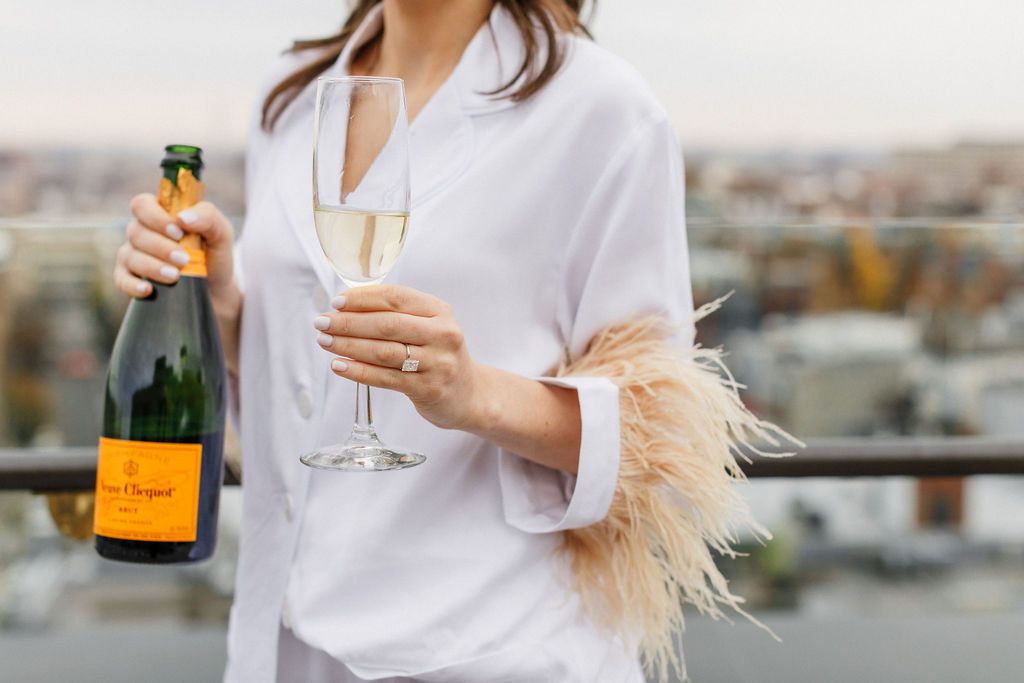 bride pouring champagne on rooftop in wedding pajamas
