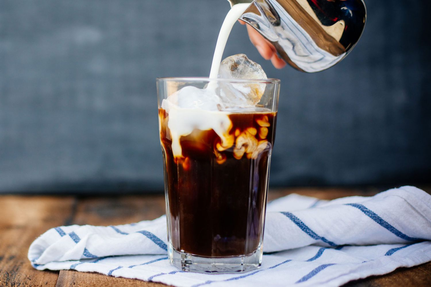 pouring milk over glass of iced coffee