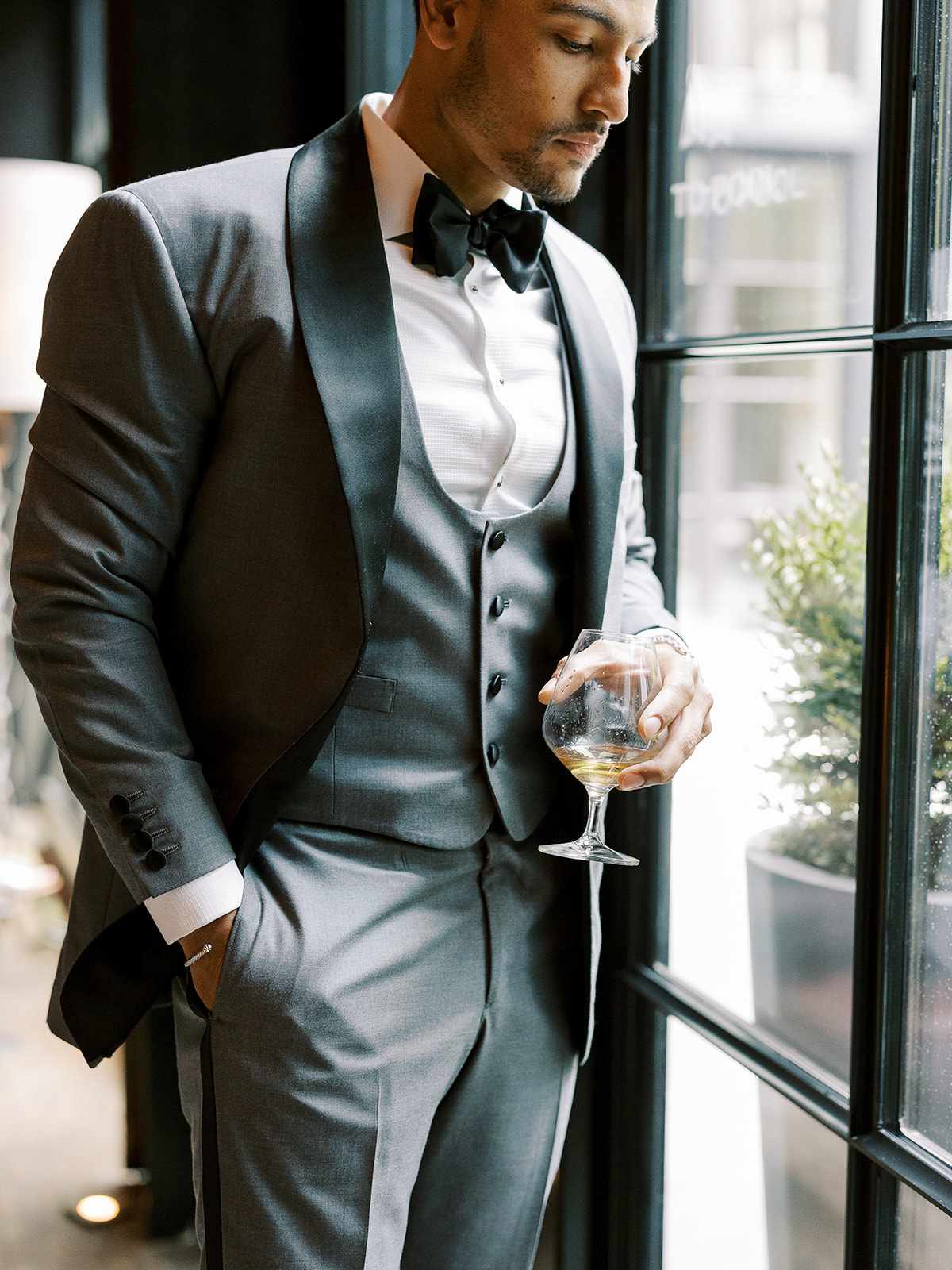 groom standing next to window with wine glass