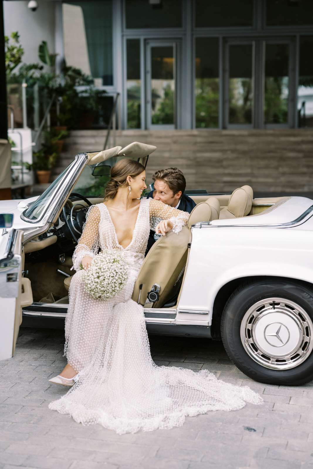 bride leaning back onto groom sitting in white vintage car