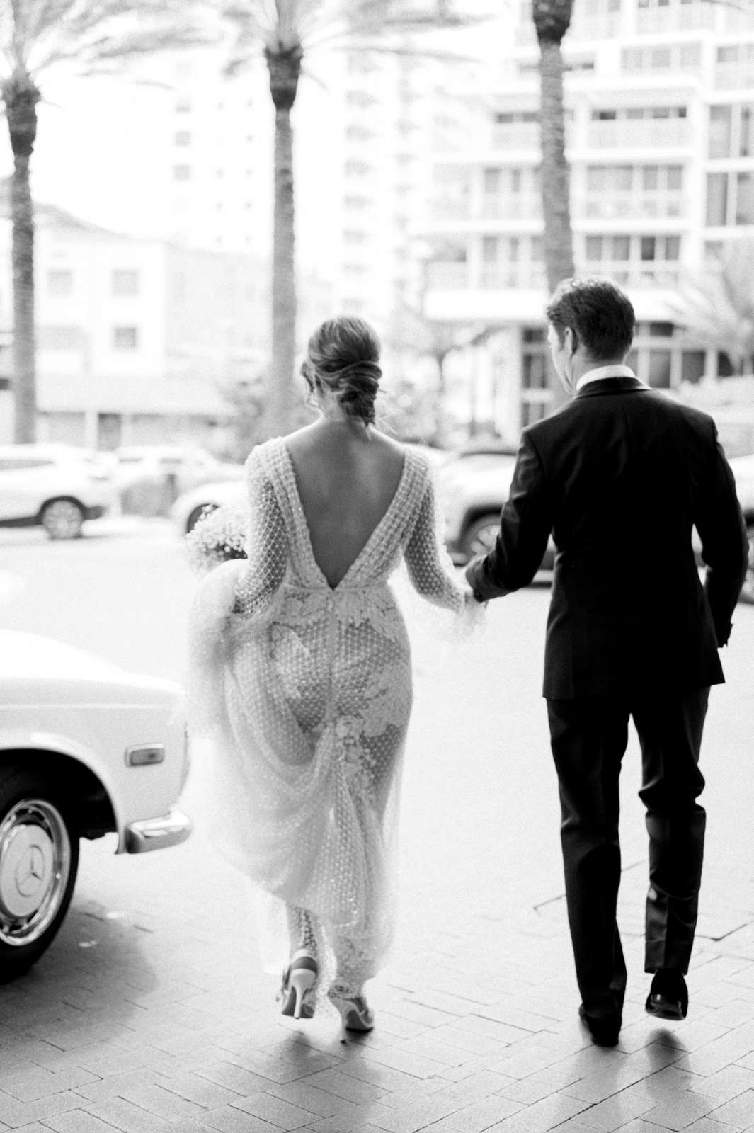 bride and groom hold hands walking toward white vintage car
