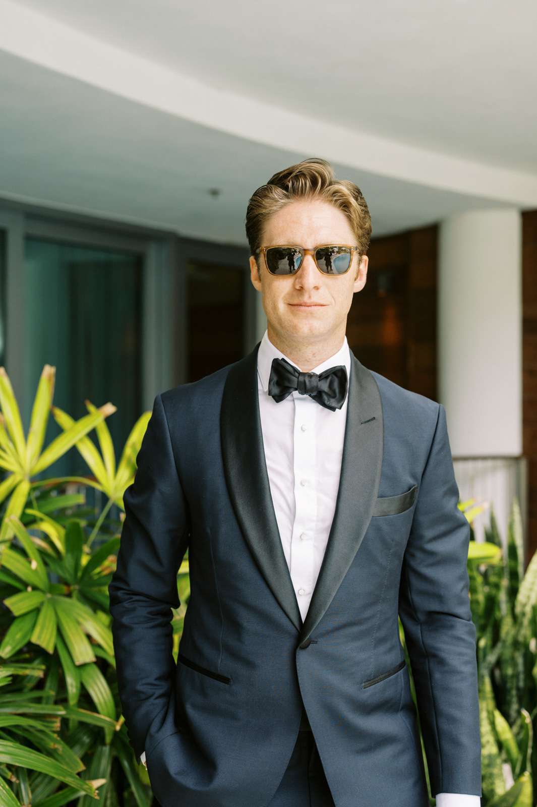 groom wearing a navy tuxedo with black lapels and sunglasses