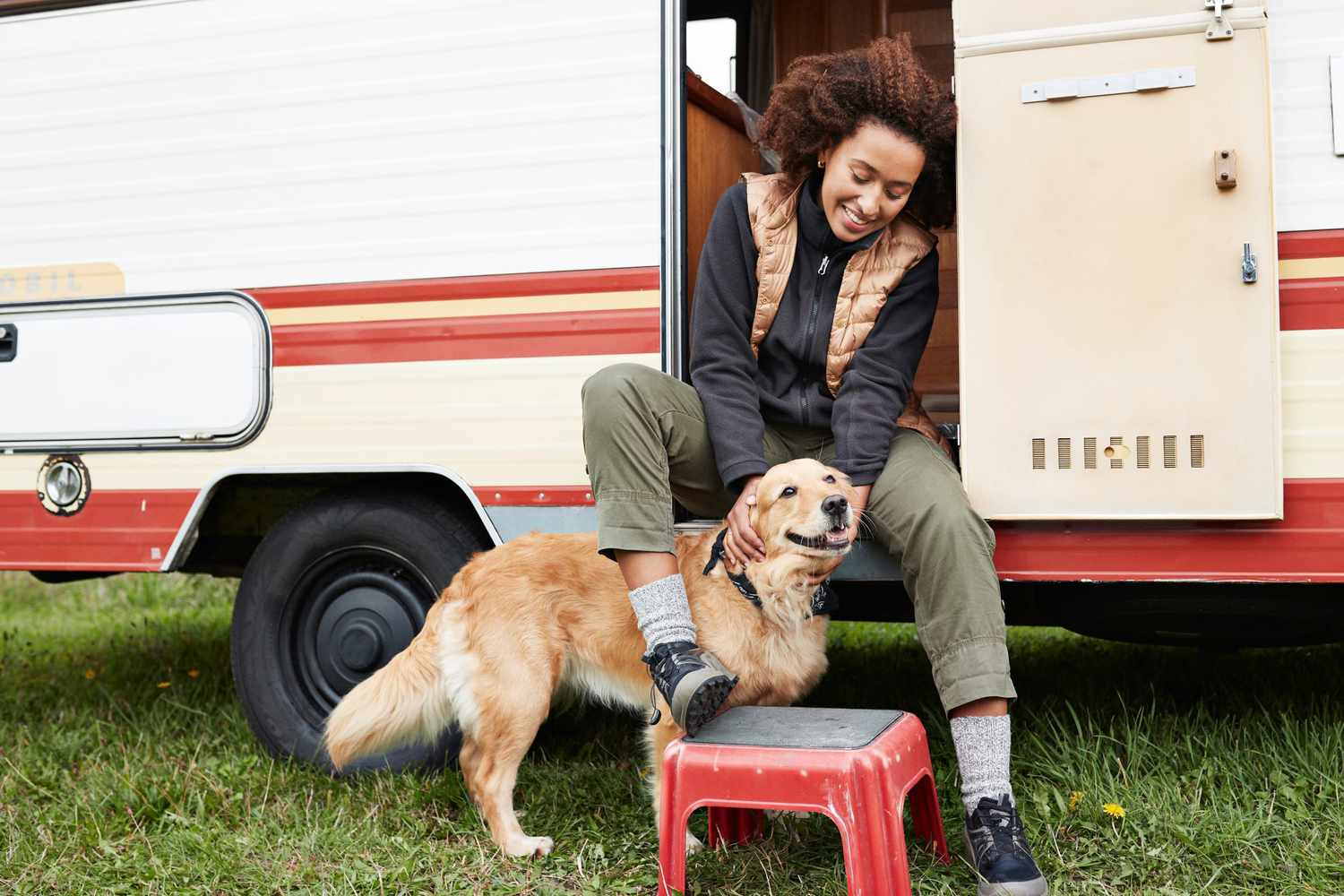 woman sitting on camper van step petting golden retriever dog