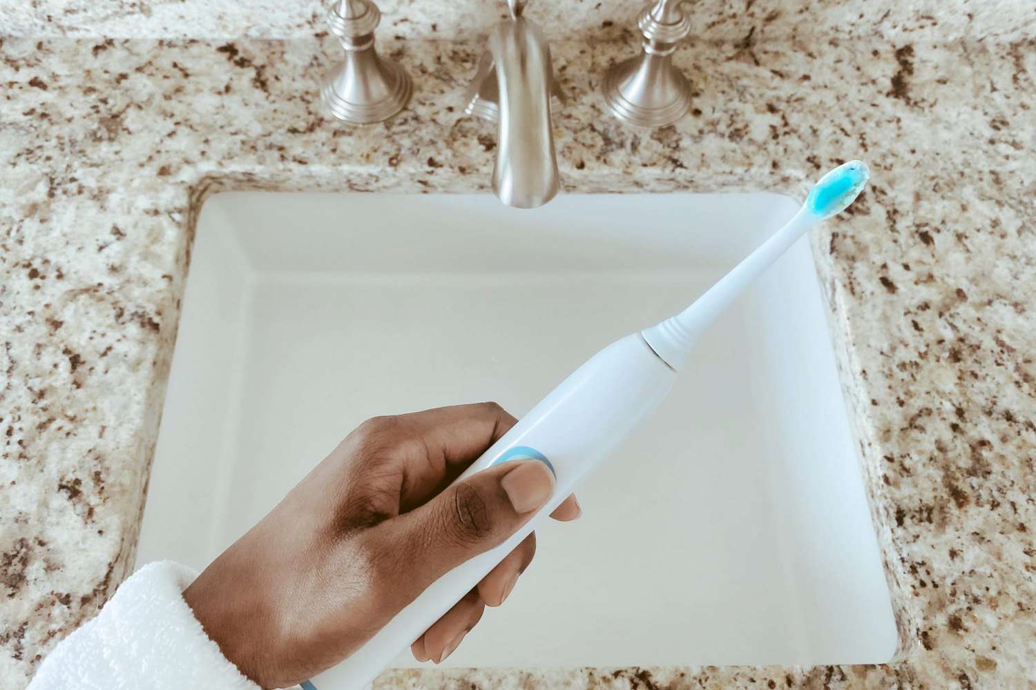 holding electric toothbrush over sink