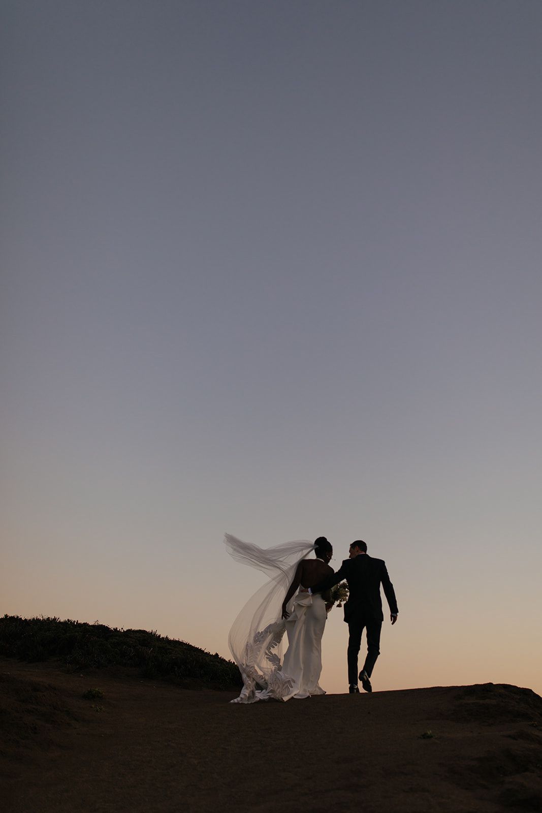 bride and groom walking toward the sunset
