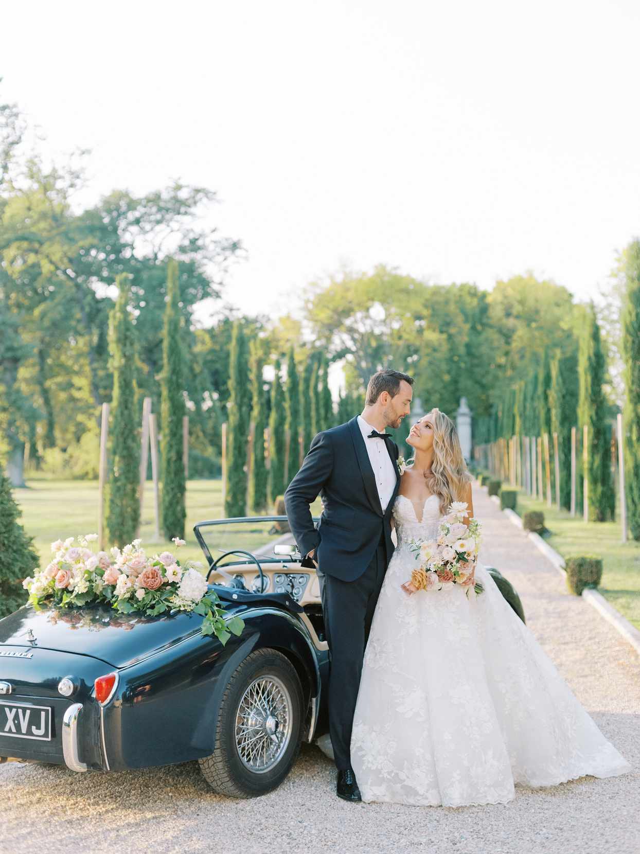 bride and groom looking at each other next to black vintage car