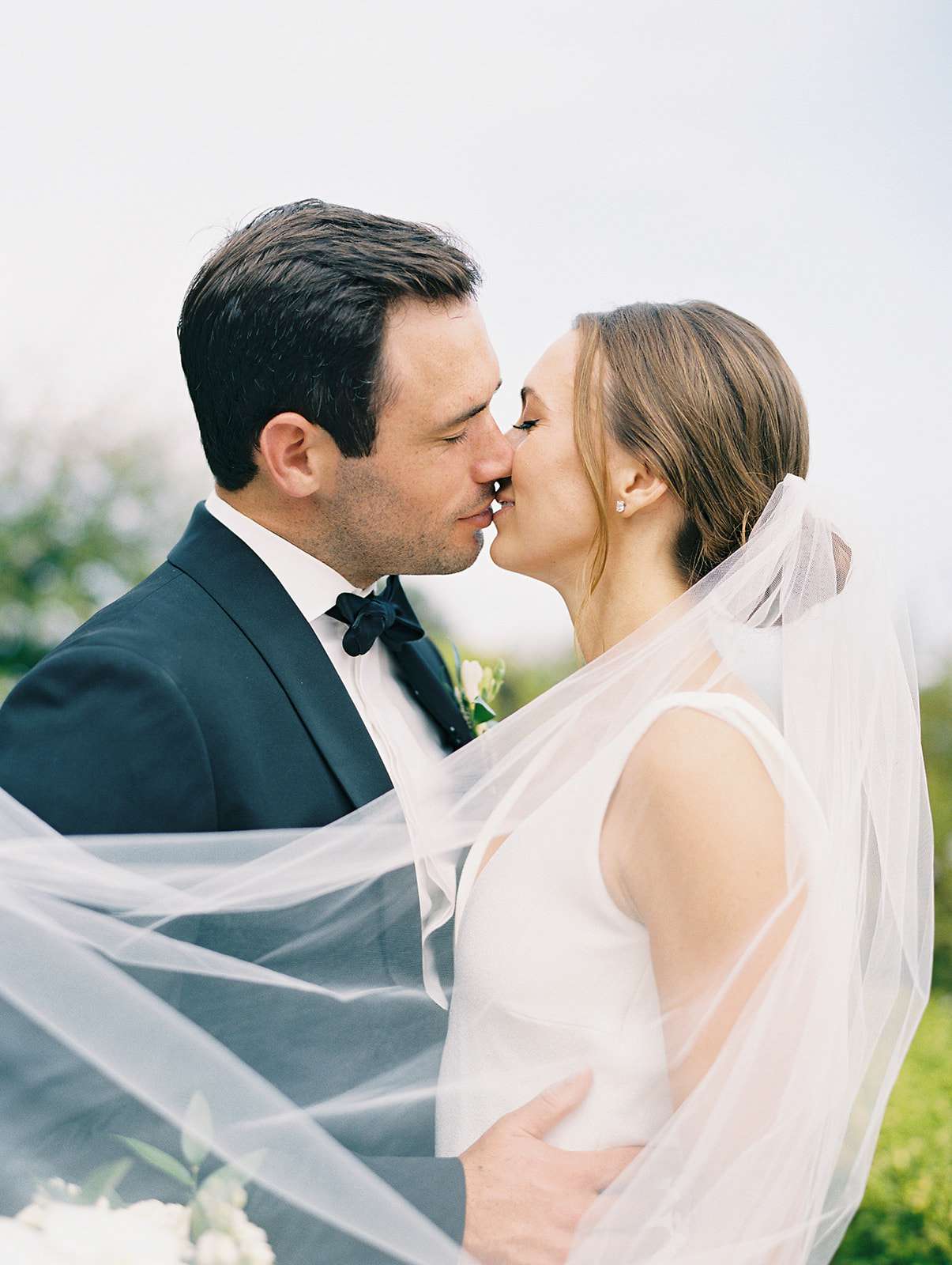 couple kissing with bride's veil flowing in the wind