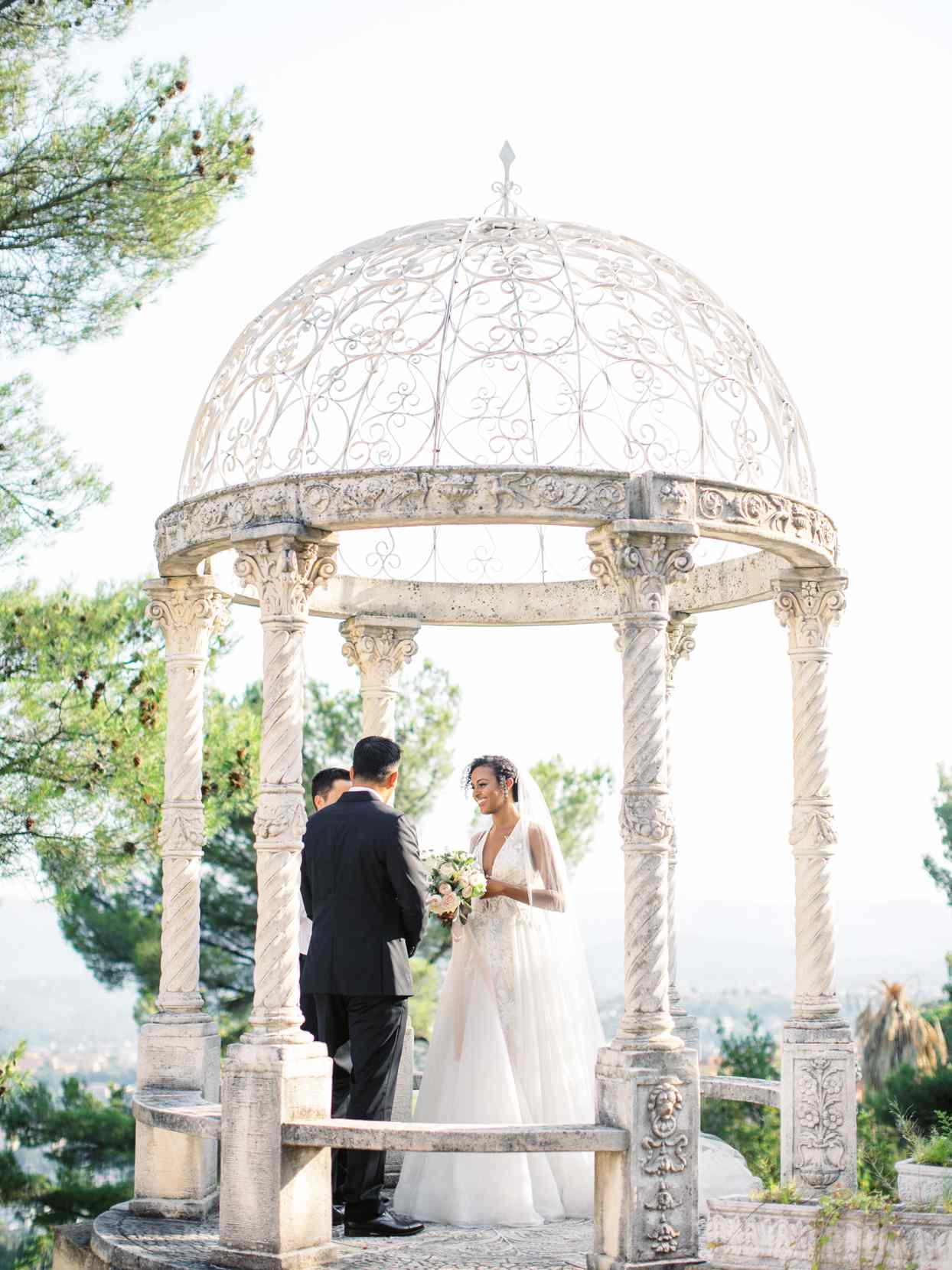 bride and groom exchanging vows beneath white stone gazebo