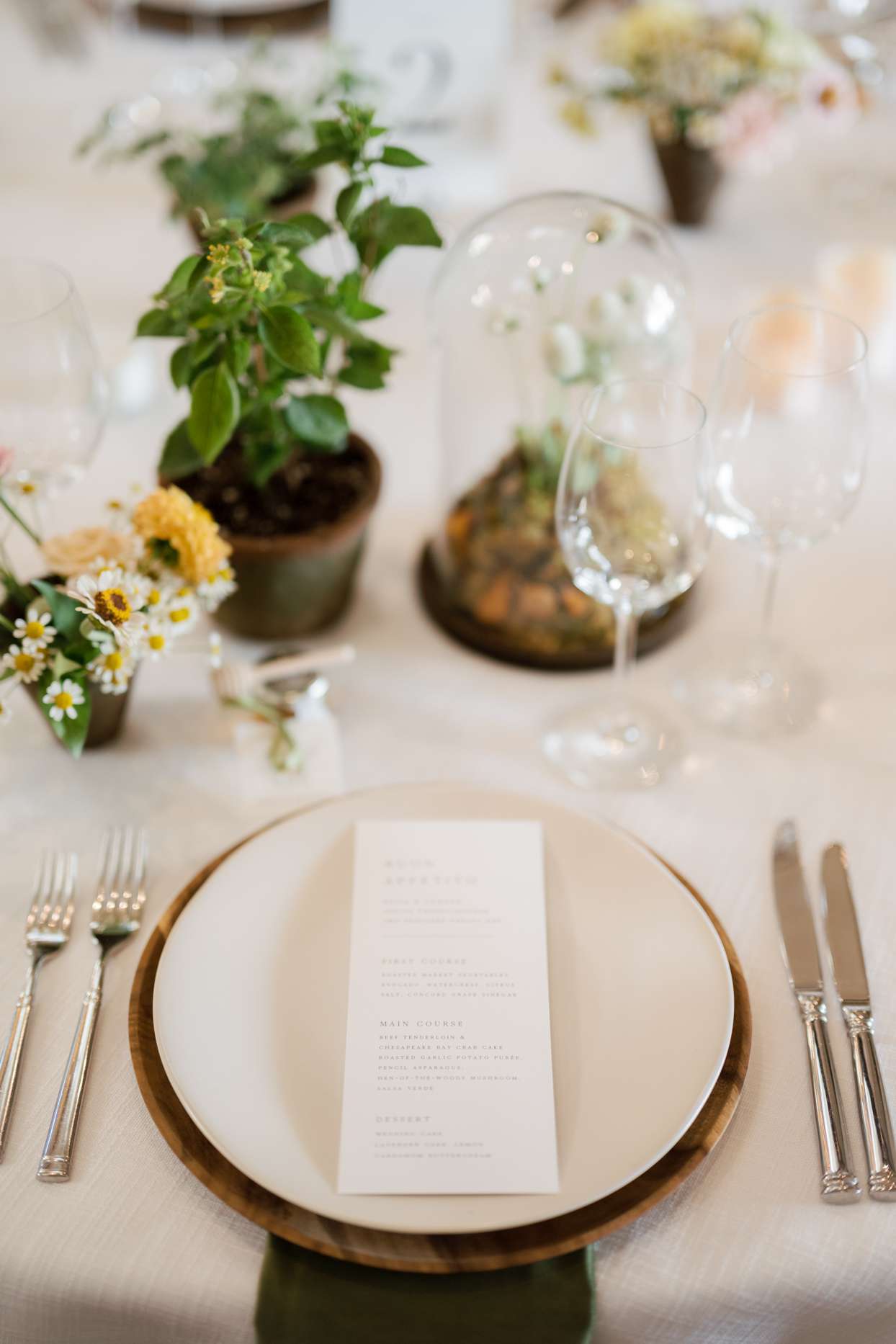 table setting with brown wooden charger and greenery centerpieces
