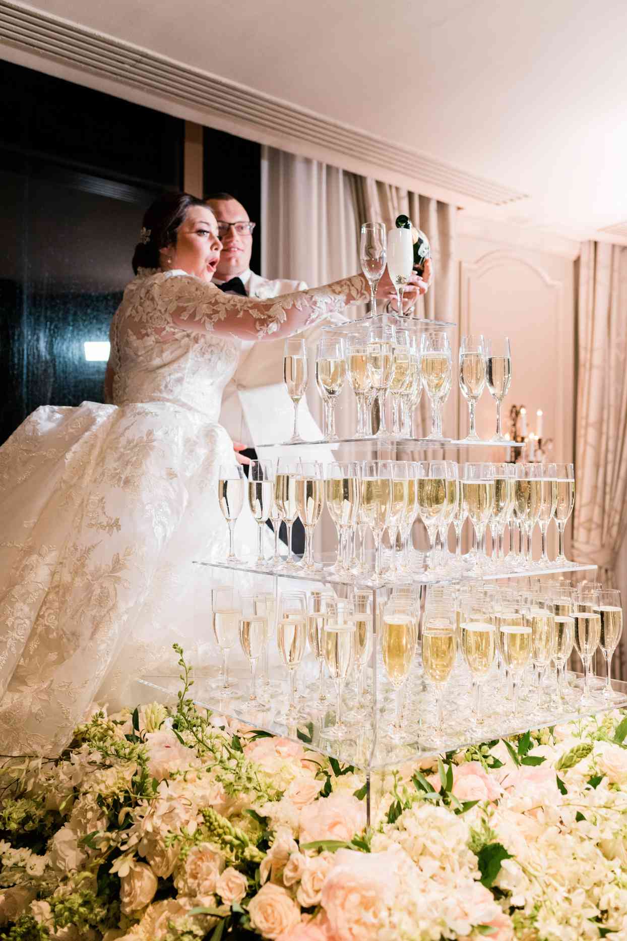 bride and groom pouring champagne tower surrounded by flowers