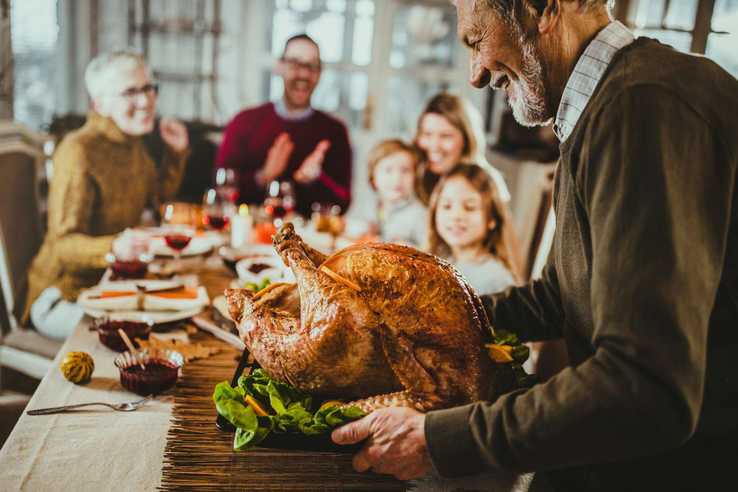 man placing thanksgiving turkey on table surrounded by family