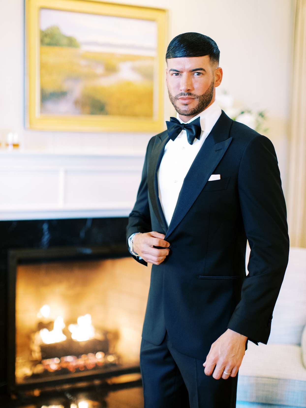 groom in black suit and bowtie in front of fireplace